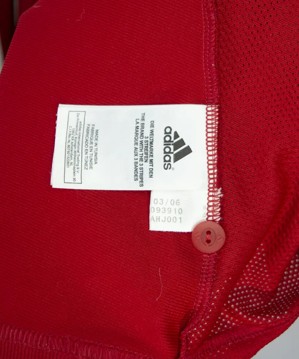 Maillot domicile rouge et blanc du bayern de la saison 2006-2007. On peut retrouver l'équipementier adidas et le sponsor t com. On peut voir l'étiquette comportant les numéros 093910