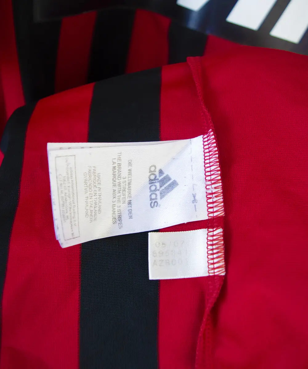 Maillot retro et vintage authentique de l'ac milan lors de la saison 2007 2008. Le maillot est de couleur rouge et noir, on peut retrouver l'équipementier adidas et le sponsor bwin. Le maillot est floqué du numéro 99 Ronaldo. Sur cette photo on peut voir l'étiquette d'authenticité du maillot comportant les numéros 695041
