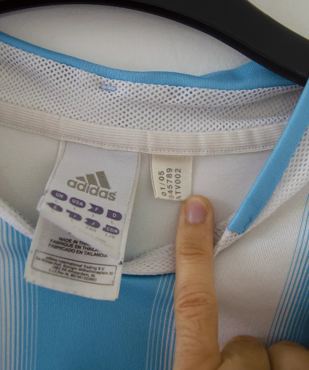 Maillot de foot authentique de l'argentine de la saison 2004-2005. Le maillot est de couleur bleu ciel et blanc. On peut retrouver l'équipementier adidas. Sur cette photo on peut voir l'étiquette d'authenticité comportant les numéros 645789