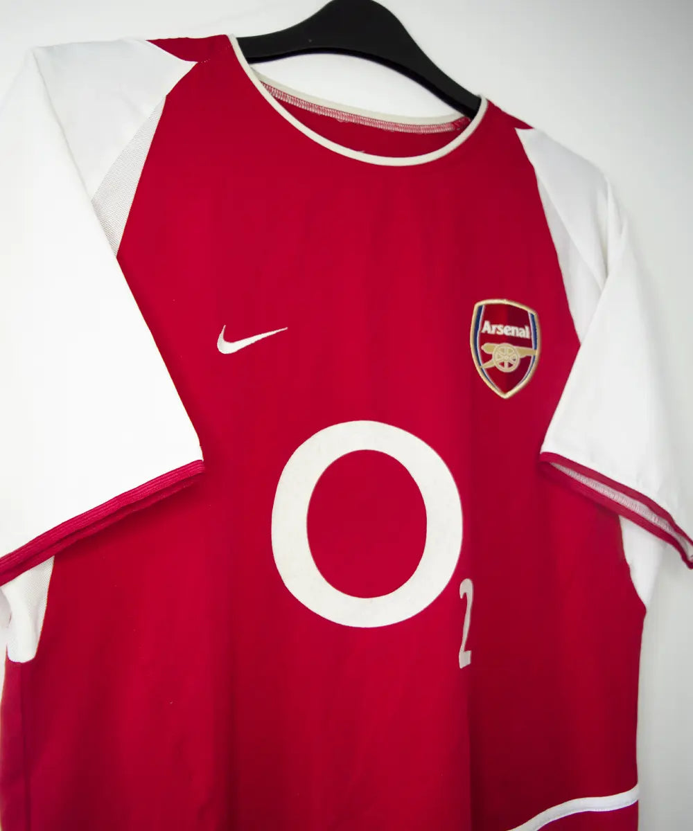 Maillot domicile Arsenal rouge et blanc de la saison 2002-2004. On peut retrouver l'équipementier nike et le sponsor O2.