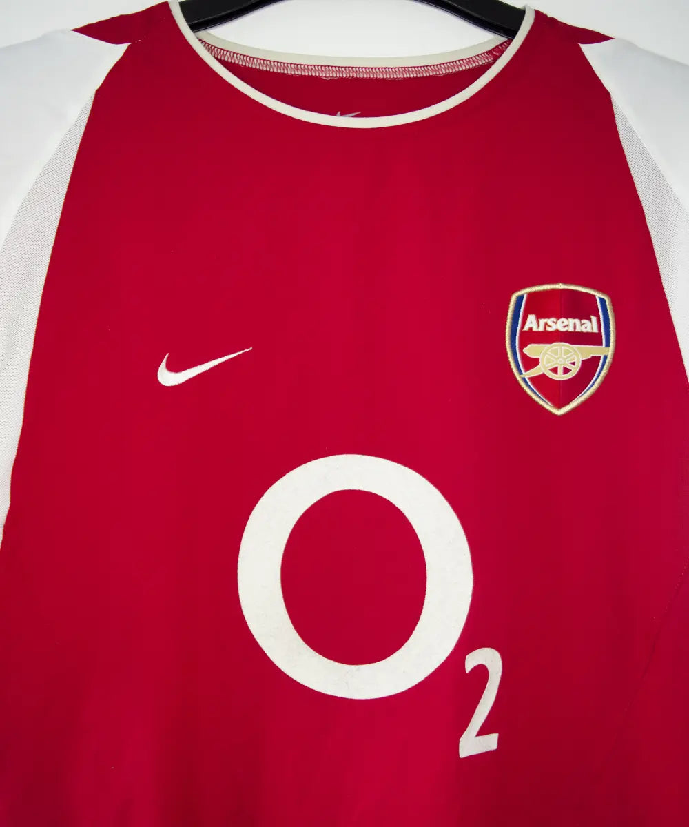 Maillot domicile Arsenal rouge et blanc de la saison 2002-2004. On peut retrouver l'équipementier nike et le sponsor O2.