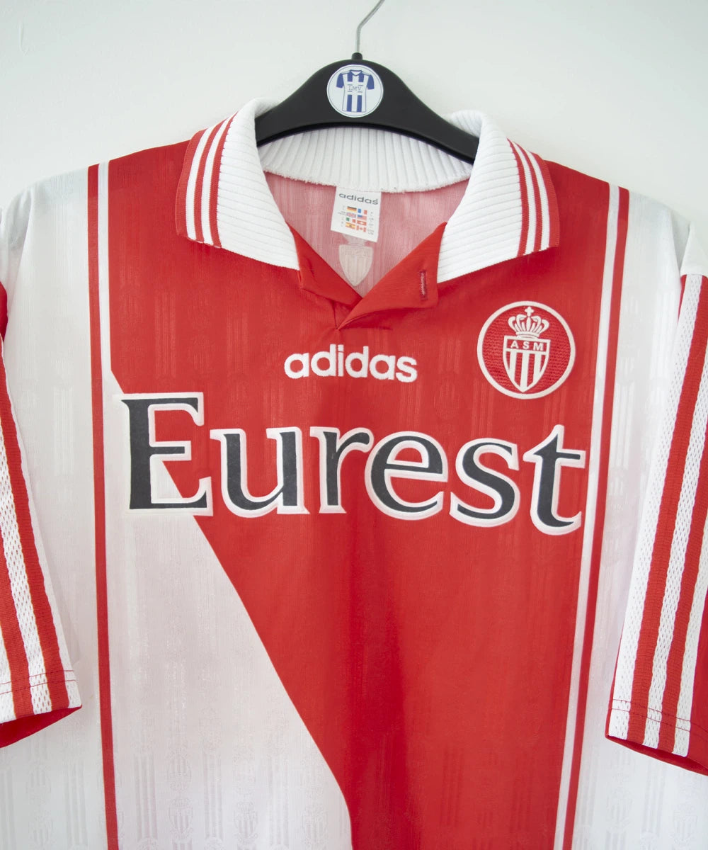 Maillot de foot vintage domicile rouge et blanc de l'AS Monaco de la saison 1996/1998. On peut retrouver l'équipementier adidas et le sponsor Eurest. Il s'agit d'un maillot authentique
