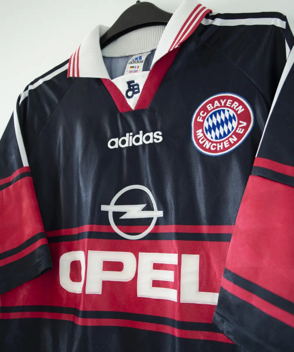 Maillot domicile noir rouge et blanc du bayern munich de la saison 1997-1998. On peut retrouver l'équipementier adidas et le sponsor opel. Le maillot est floqué du numéro 3 Lizarazu