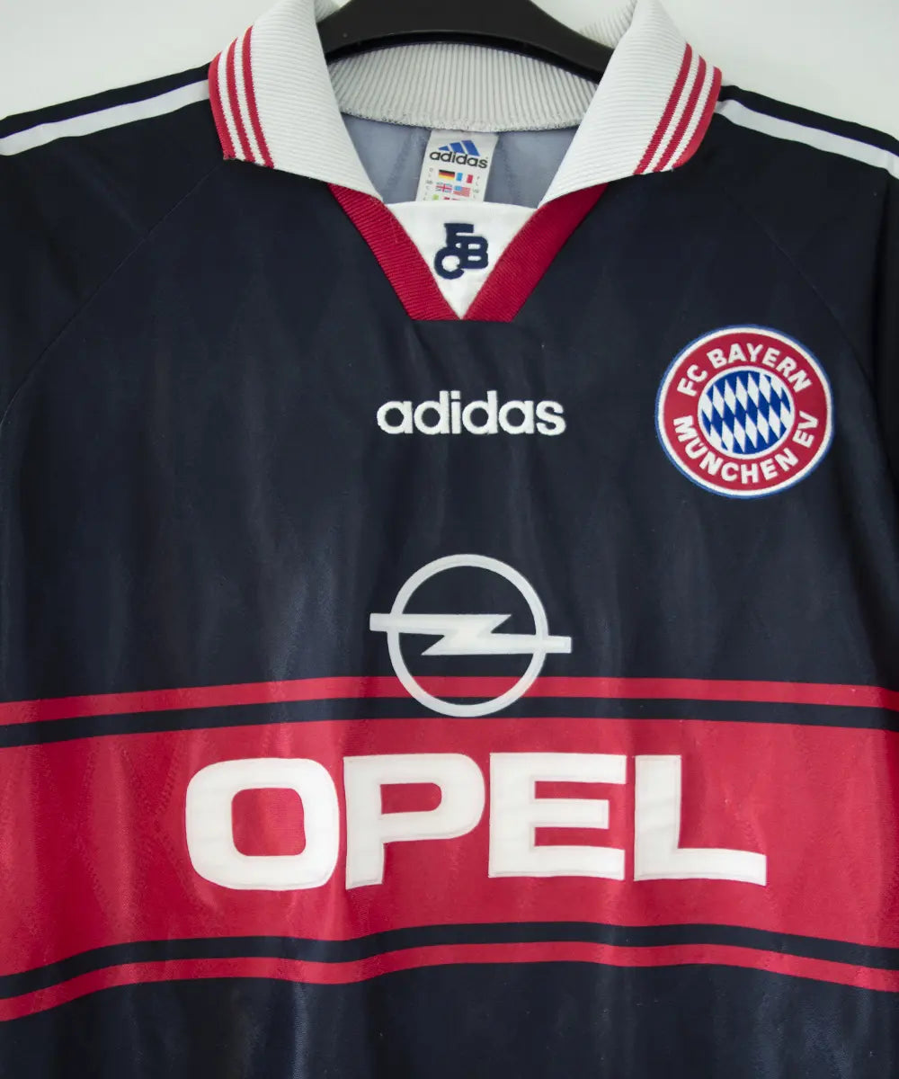 Maillot domicile noir rouge et blanc du bayern munich de la saison 1997-1998. On peut retrouver l'équipementier adidas et le sponsor opel. Le maillot est floqué du numéro 3 Lizarazu