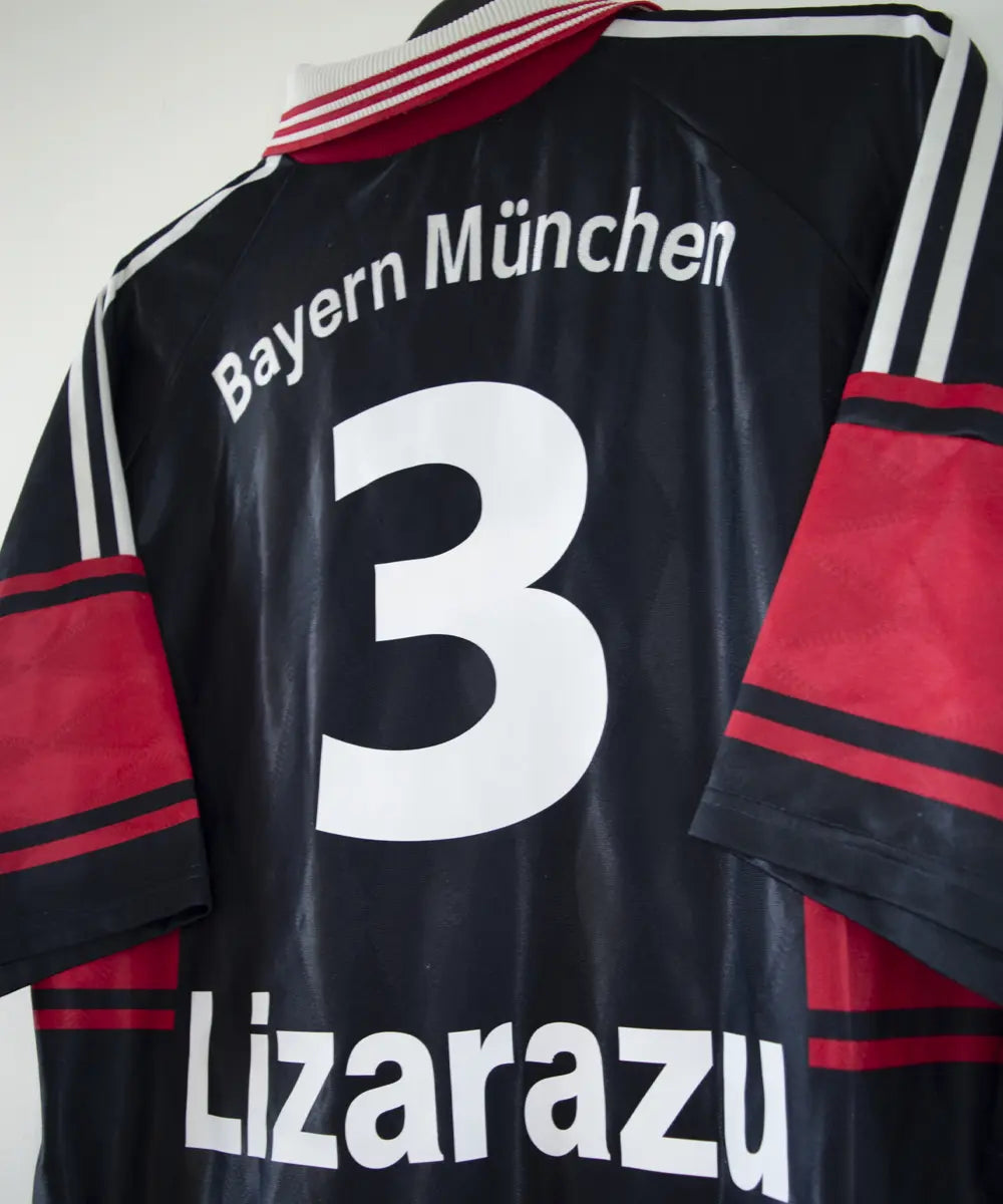 Maillot domicile noir rouge et blanc du bayern munich de la saison 1997-1998. On peut retrouver l'équipementier adidas et le sponsor opel. Le maillot est floqué du numéro 3 Lizarazu