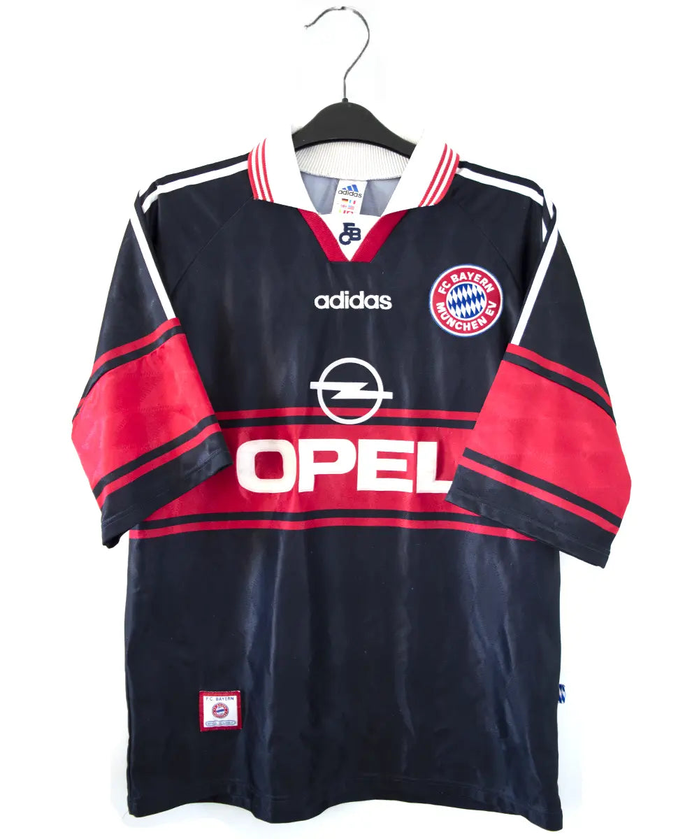 Maillot domicile noir rouge et blanc du bayern munich de la saison 1997-1998. On peut retrouver l'équipementier adidas et le sponsor opel. Le maillot est floqué du numéro 3 Lizarazu