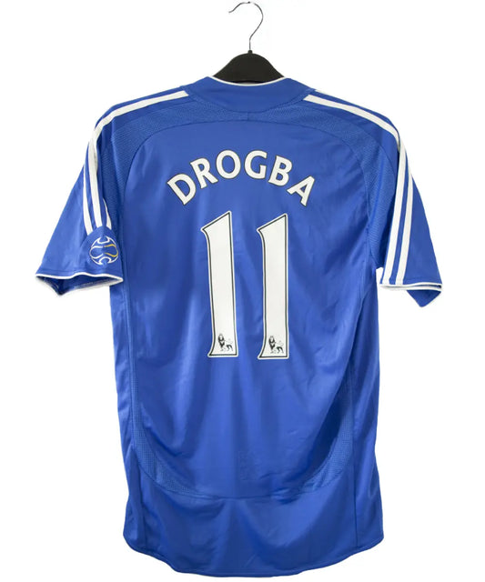 Maillot de foot vintage bleu domicile de chelsea de la saison 2006-2008. On peut retrouver l'équipementier adidas et le sponsor samsung. Le maillot est floqué du numéro 11 Didier Drogba. Le maillot possède l'étiquette 061230