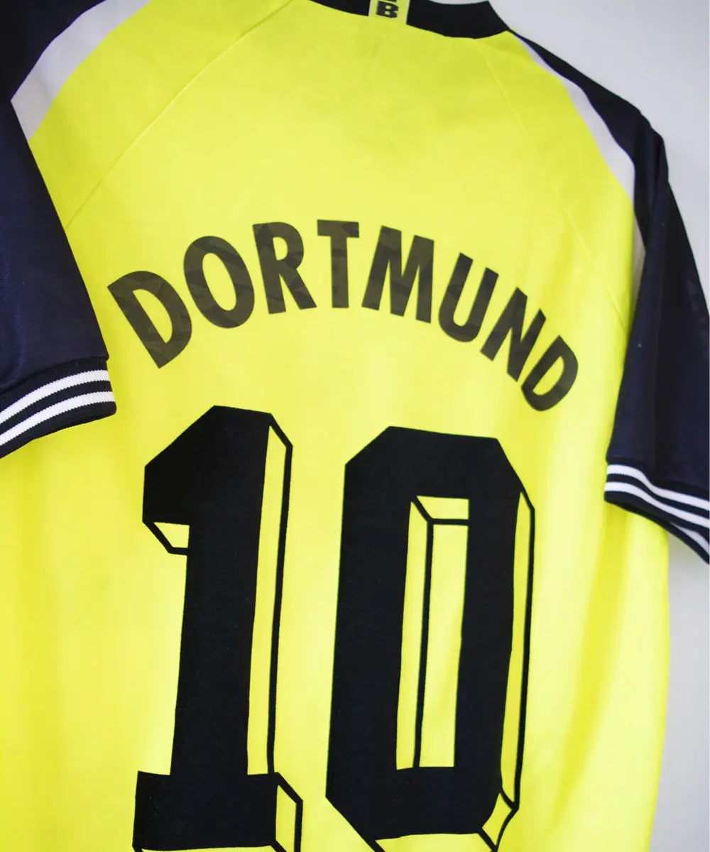 Maillot domicile du Borussia Dortmund de la saison 1995-1996. Le maillot est de couleur jaune et noir. On peut retrouver sur le maillot le sponsor die continentale et l'équipementier nike. Le maillot est floqué du numéro 10 Frank Möller. Sur cette phoo on peut apercevoir le flocage de côté