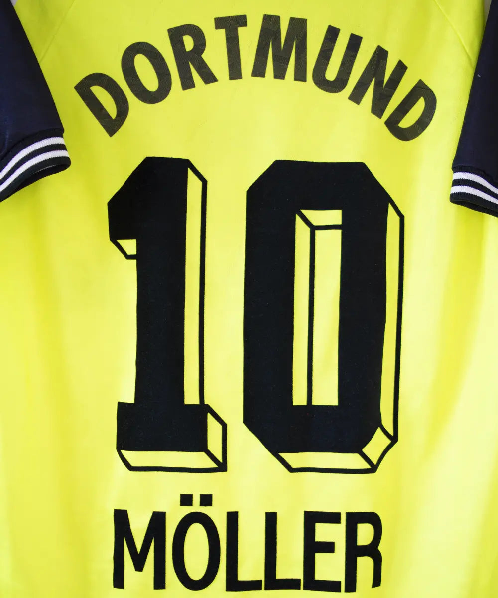 Maillot domicile du Borussia Dortmund de la saison 1995-1996. Le maillot est de couleur jaune et noir. On peut retrouver sur le maillot le sponsor die continentale et l'équipementier nike. Le maillot est floqué du numéro 10 Frank Möller. Sur cette photo on peut apercevoir le flocage de près.