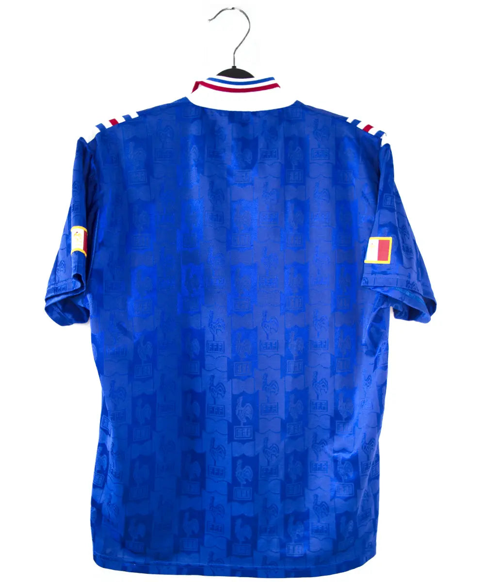 Maillot domicile de l'équipe de france 1996 de couleur bleu blanc et rouge. On peut retrouver l'équipementier adidas et le coq sans étoile