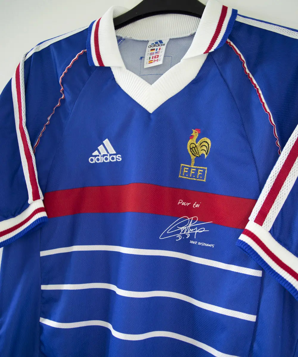 Maillot domicile de l'équipe de france 1998. Le maillot est de couleur bleu, blanc et rouge. On peut retrouver l'équipementier adidas et le coq sans étoile. Le maillot est signé Didier Deschamps