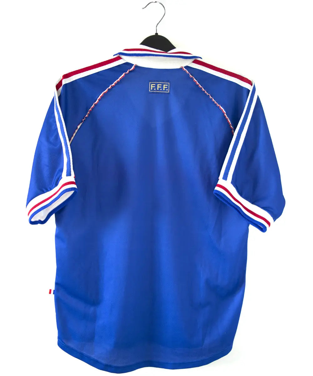 Maillot domicile de l'équipe de france 1998. Le maillot est de couleur bleu, blanc et rouge. On peut retrouver l'équipementier adidas et le coq sans étoile. Le maillot est signé Didier Deschamps