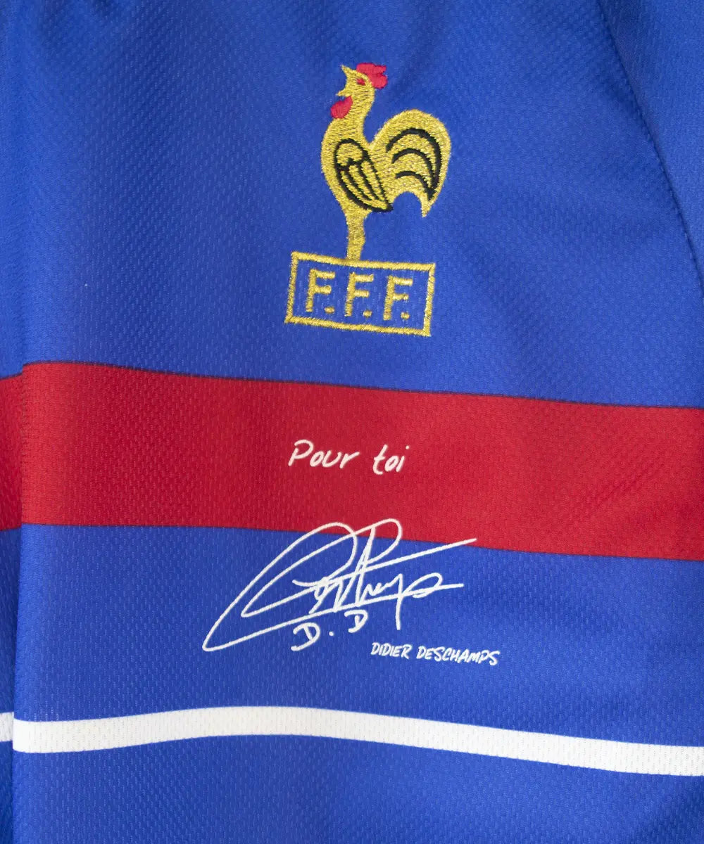 Maillot domicile de l'équipe de france 1998. Le maillot est de couleur bleu, blanc et rouge. On peut retrouver l'équipementier adidas et le coq sans étoile. Le maillot est signé Didier Deschamps