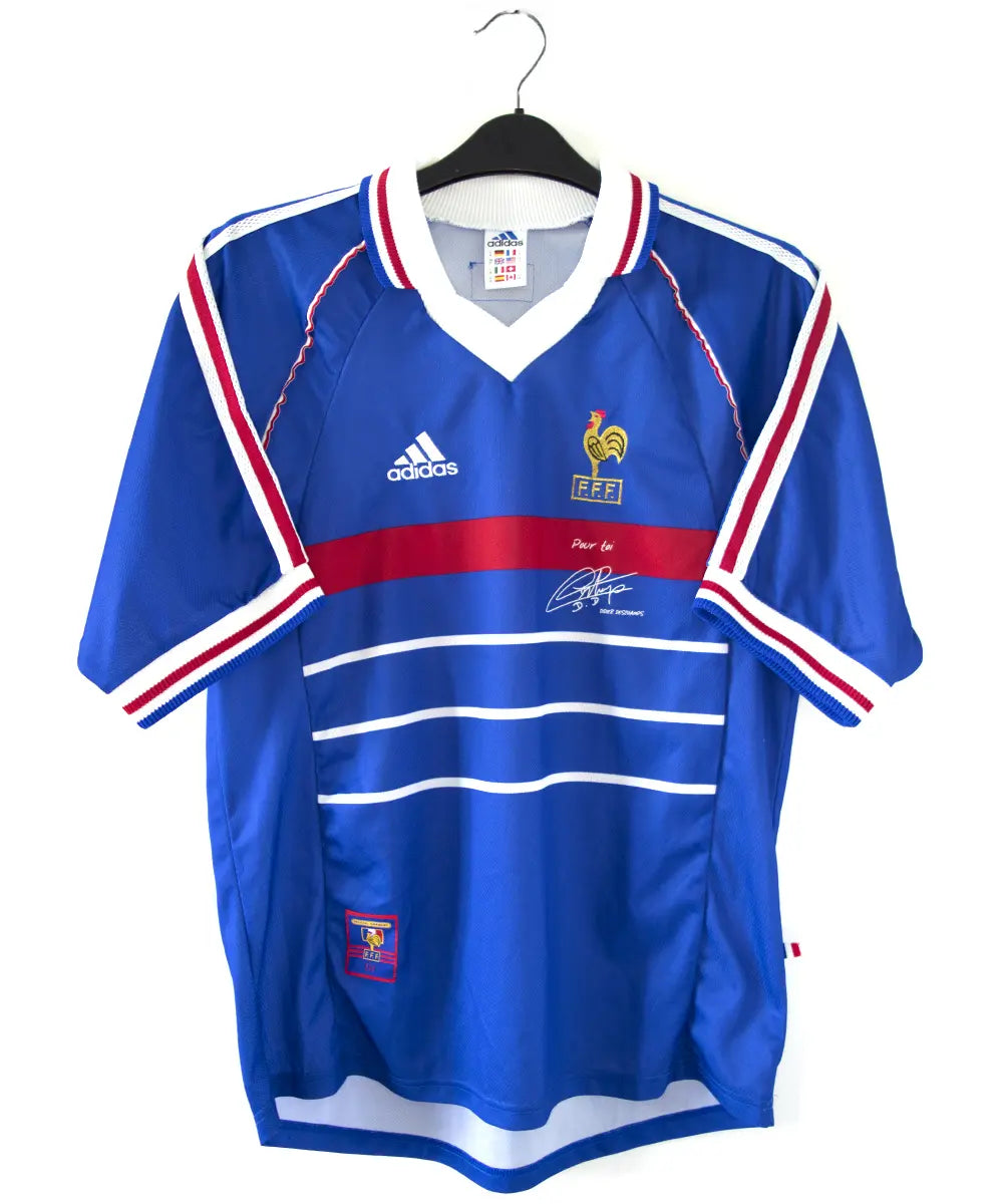 Maillot domicile de l'équipe de france 1998. Le maillot est de couleur bleu, blanc et rouge. On peut retrouver l'équipementier adidas et le coq sans étoile. Le maillot est signé Didier Deschamps