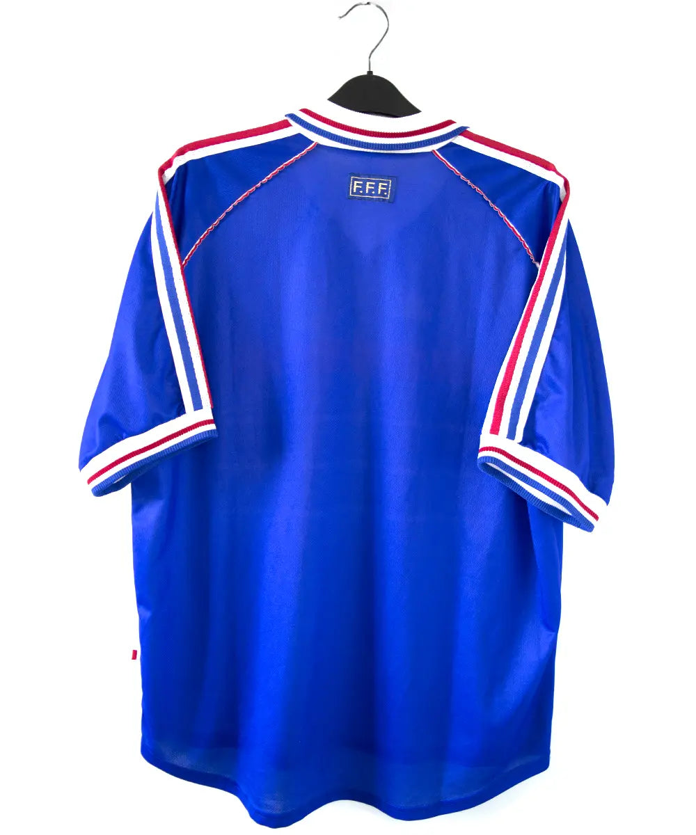 Maillot domicile équipe de france 1998 signé Zidane. Le maillot est de couleur bleu. On peut retrouver l'équipementier adidas et le coq sans étoile. Sur cette photo on peut apercevoir le maillot de dos