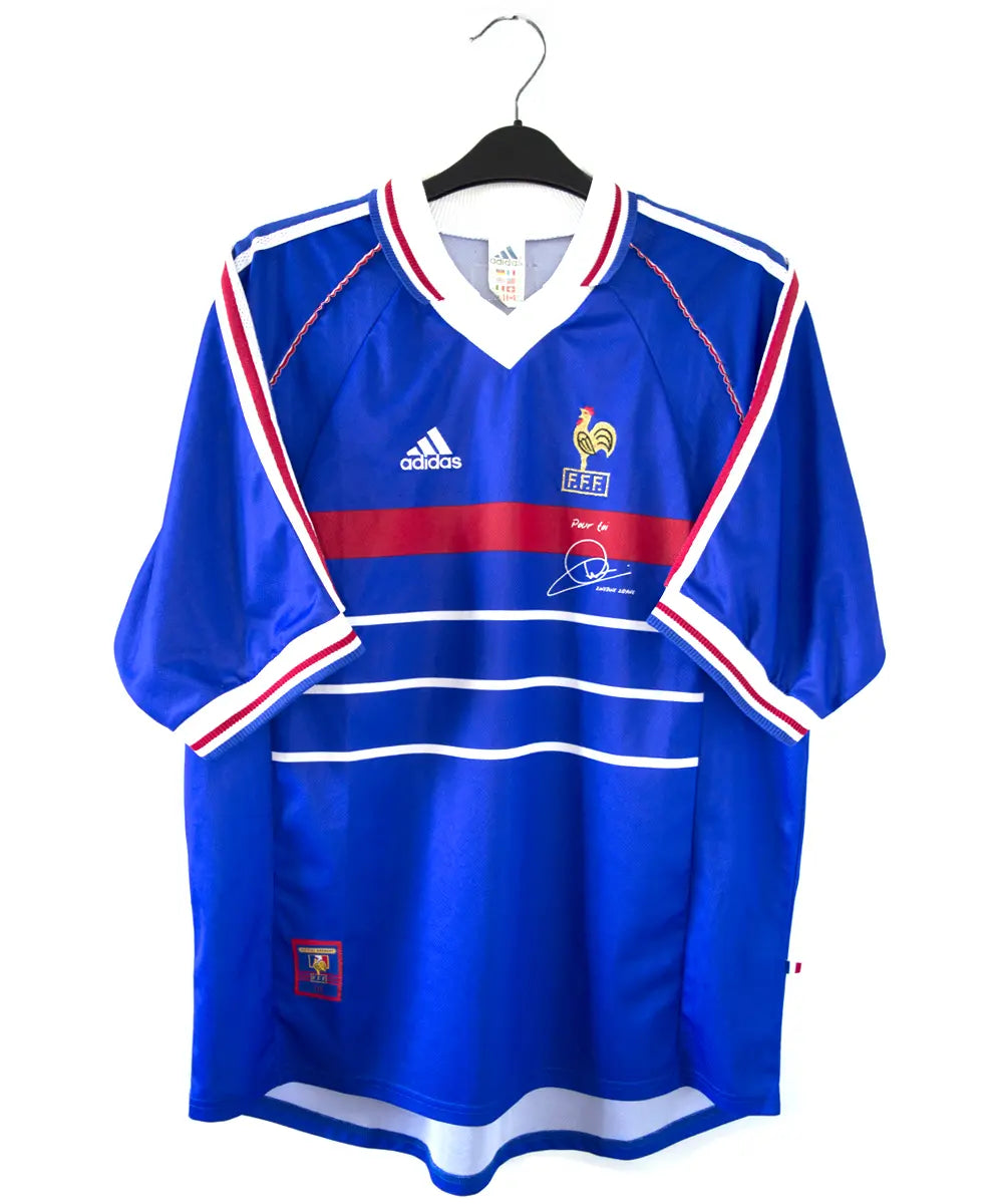 Maillot domicile équipe de france 1998 signé Zidane. Le maillot est de couleur bleu. On peut retrouver l'équipementier adidas et le coq sans étoile.