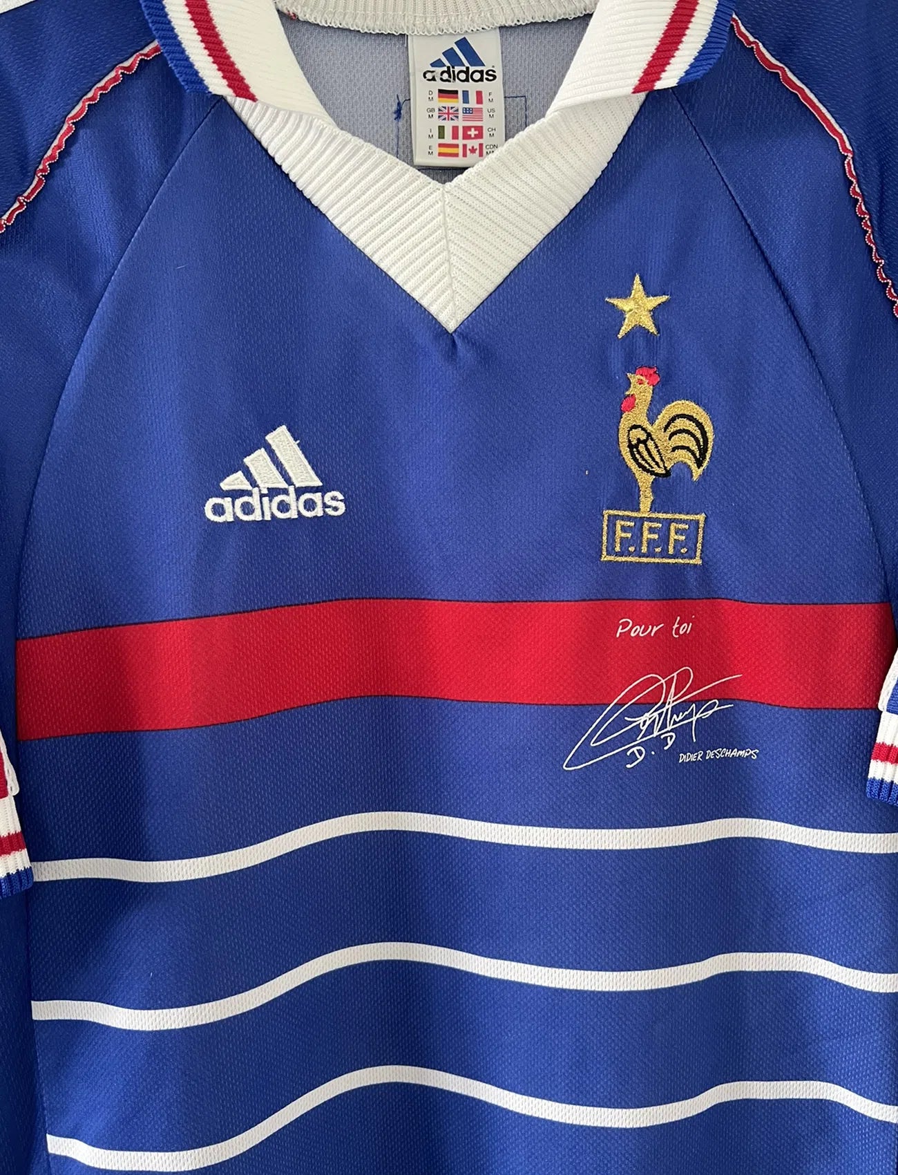 Maillot de foot vintage de l'équipe de france bleu blanc et rouge. Il s'agit du maillot domicile de la coupe du monde 1998. On peut retrouver l'équipementier adidas et le coq avec l'étoile. Le maillot possède la signature pour toi de Didier Deschamps