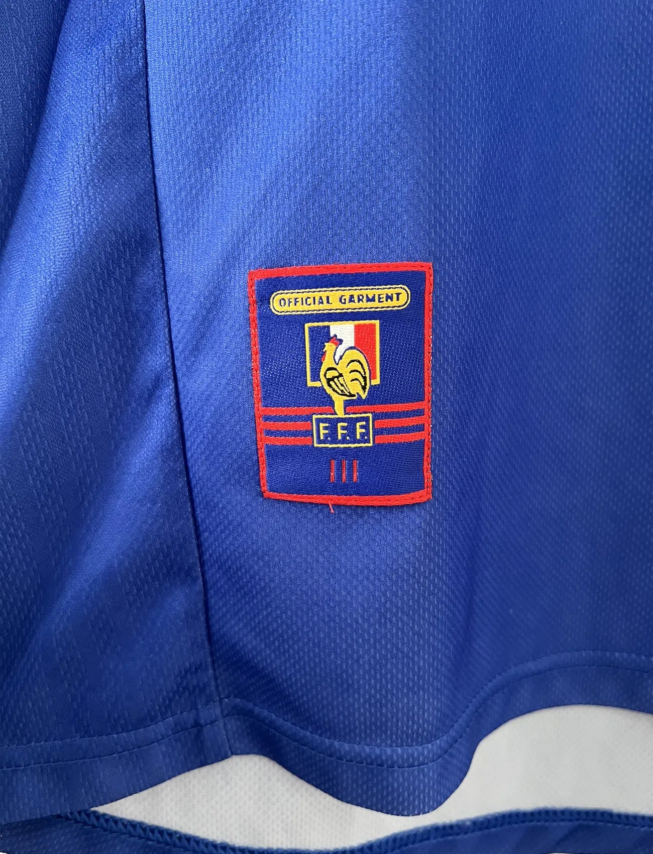 Maillot de foot vintage de l'équipe de france bleu blanc et rouge. Il s'agit du maillot domicile de la coupe du monde 1998. On peut retrouver l'équipementier adidas et le coq avec l'étoile. Le maillot possède la signature pour toi de Didier Deschamps