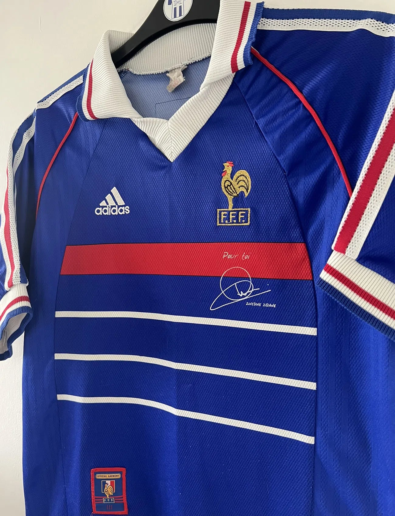 Maillot de foot vintage de l'équipe de france bleu blanc et rouge. Il s'agit du maillot domicile de la coupe du monde 1998. On peut retrouver l'équipementier adidas et le coq sans l'étoile. Le maillot possède la signature pour toi de Zinedine Zidane