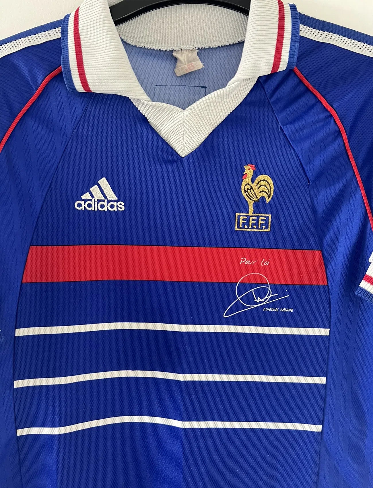 Maillot de foot vintage de l'équipe de france bleu blanc et rouge. Il s'agit du maillot domicile de la coupe du monde 1998. On peut retrouver l'équipementier adidas et le coq sans l'étoile. Le maillot possède la signature pour toi de Zinedine Zidane