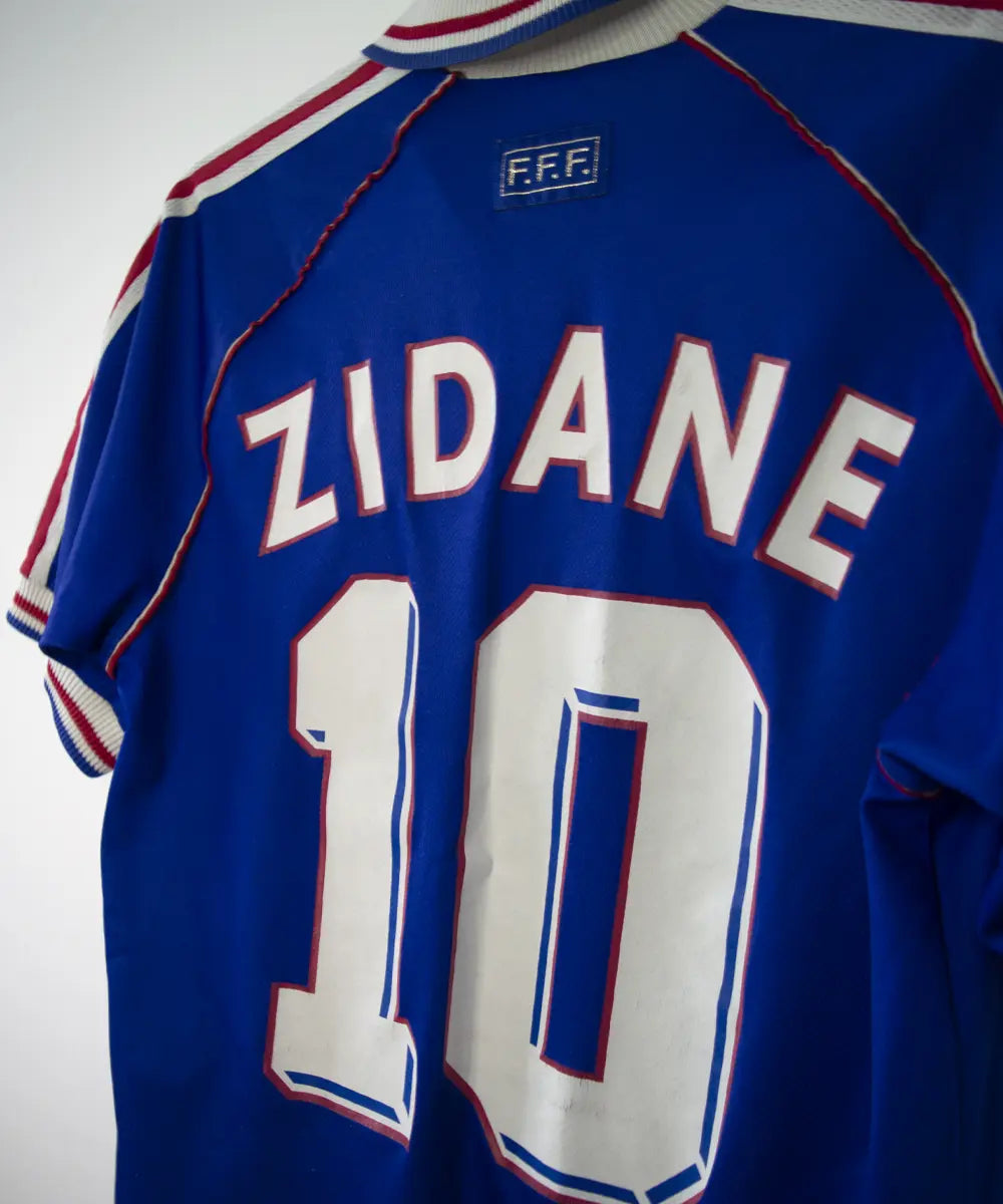 Maillot de foot vintage bleu blanc et rouge de l'équipe de france 1998. On peut retrouver l'équipementier adidas. Le maillot est floqué du numéro 10 Zinedine Zidane