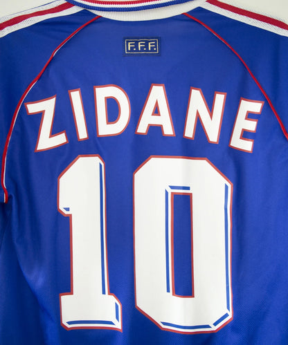 Maillot vintage domicile bleu, blanc et rouge de l'équipe de france 1998. On peut retrouver l'équipementier adidas. Le maillot est floqué du numéro 10 Zinedine Zidane avec le flocage à l'avant et à l'arrière du maillot. Il s'agit d'un maillot authentique d'époque