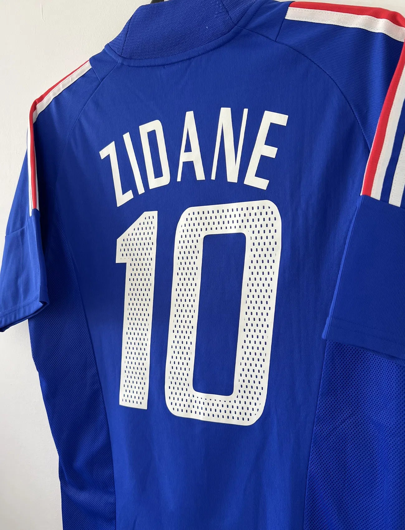 Maillot de foot vintage domicile de l'Equipe de France 2002. Le maillot est de couleur bleu, blanc et rouge. On peut retrouver l'équipementier adidas et le flocage de Zinedine Zidane. Il s'agit d'un maillot authentique. Le maillot possède l'étiquette d'authenticité comportant les numéros 139531.