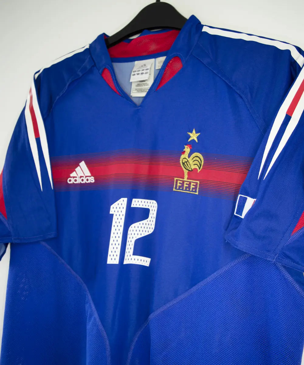 Maillot domicile bleu, blanc et rouge de l'équipe de france 2004-2006. On peut retrouver l'équipementier adidas. Le maillot est floqué du numéro 12 Thierry Henry