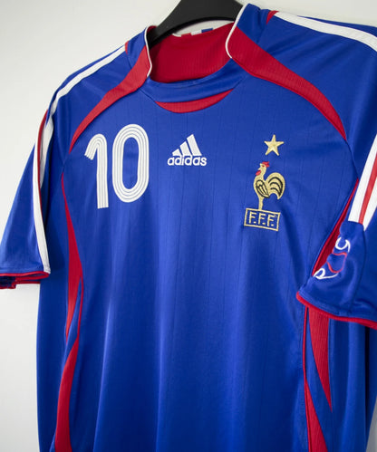 Maillot de foot vintage domicile bleu, blanc et rouge de l'équipe de france 2006. On peut retrouver l'équipementier adidas. Le maillot est floqué du numéro 10 Zinedine Zidane. Il s'agit d'un maillot authentique