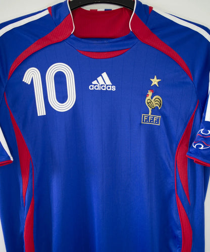 Maillot de foot vintage domicile bleu, blanc et rouge de l'équipe de france 2006. On peut retrouver l'équipementier adidas. Le maillot est floqué du numéro 10 Zinedine Zidane. Il s'agit d'un maillot authentique