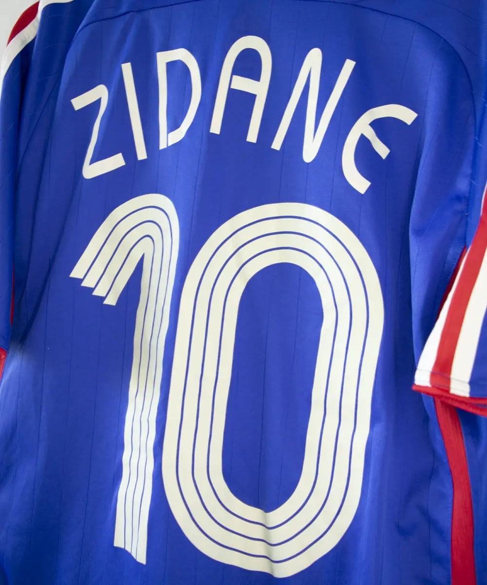 Maillot domicile de l'équipe de france porté lors de la coupe du monde 2006. Le maillot est de couleur bleu blanc et rouge. On peut retrouver l'équipementier adidas. Le maillot est floqué du numéro 10 Zinedine Zidane. Sur cette photo on peut apercevoir le flocage de côté