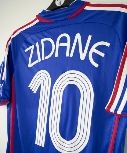 Maillot de foot vintage domicile bleu, blanc et rouge de l'équipe de france 2006. On peut retrouver l'équipementier adidas. Le maillot est floqué du numéro 10 Zinedine Zidane. Il s'agit d'un maillot authentique