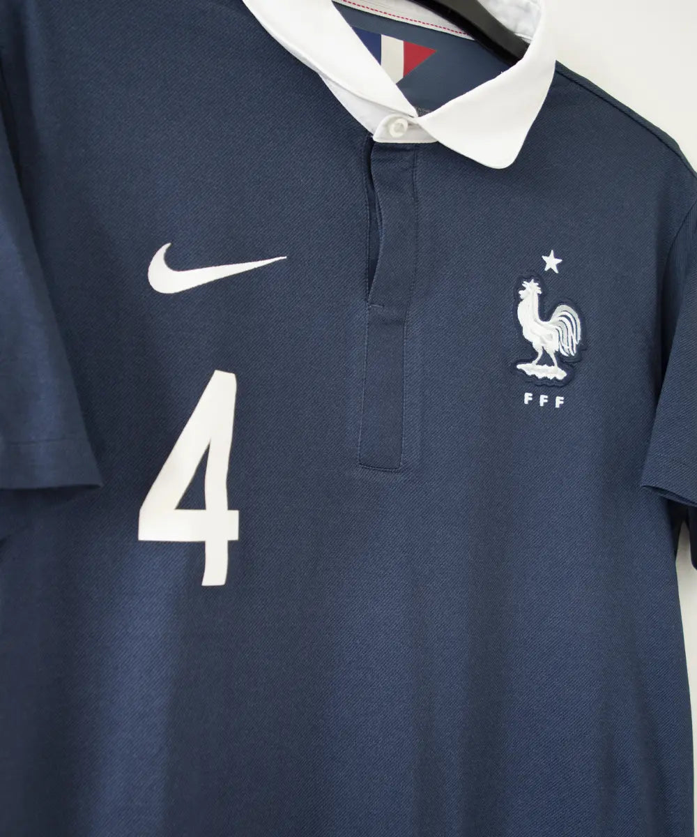 Maillot domicile équipe de france édité lors de la coupe du monde 2014. Le maillot est de couleur bleu et blanc. On peut retrouver l'équipementier nike. Le maillot est floqué du numéro 4 Varane. Sur cette photo on peut voir le devant du maillot de côté