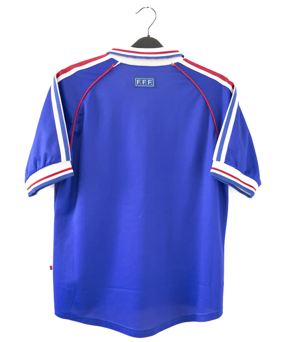 Maillot de foot de l'équipe de france 1998. Le maillot est de couleur bleu, blanc rouge. On peut retrouver l'équipementier adidas et la signature de zinedine zidane. Sur cette photo on peut voir le maillot de dos