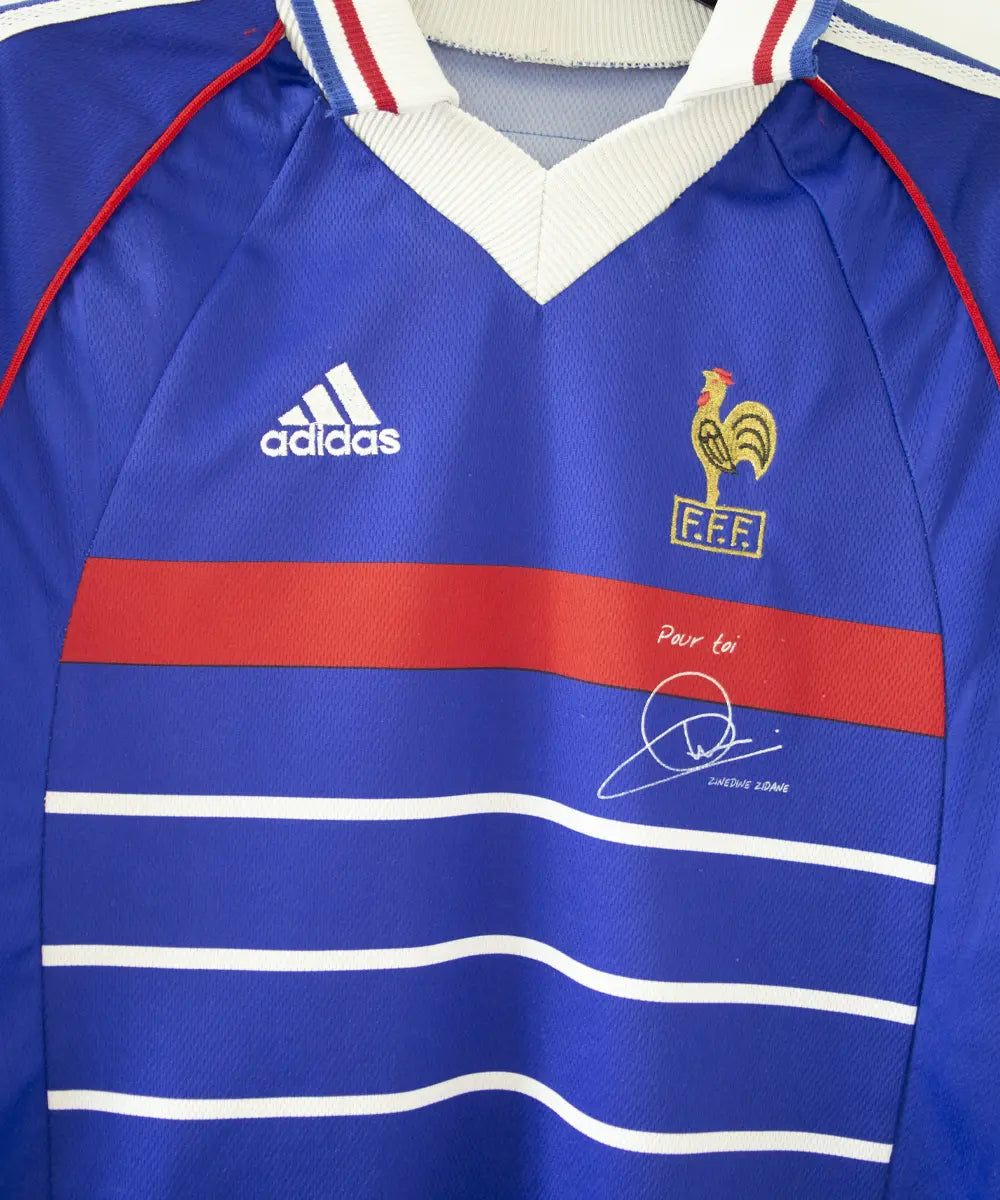 Maillot de foot de l'équipe de france 1998. Le maillot est de couleur bleu, blanc rouge. On peut retrouver l'équipementier adidas et la signature de zinedine zidane. Sur cette photo on peut voir le maillot de près