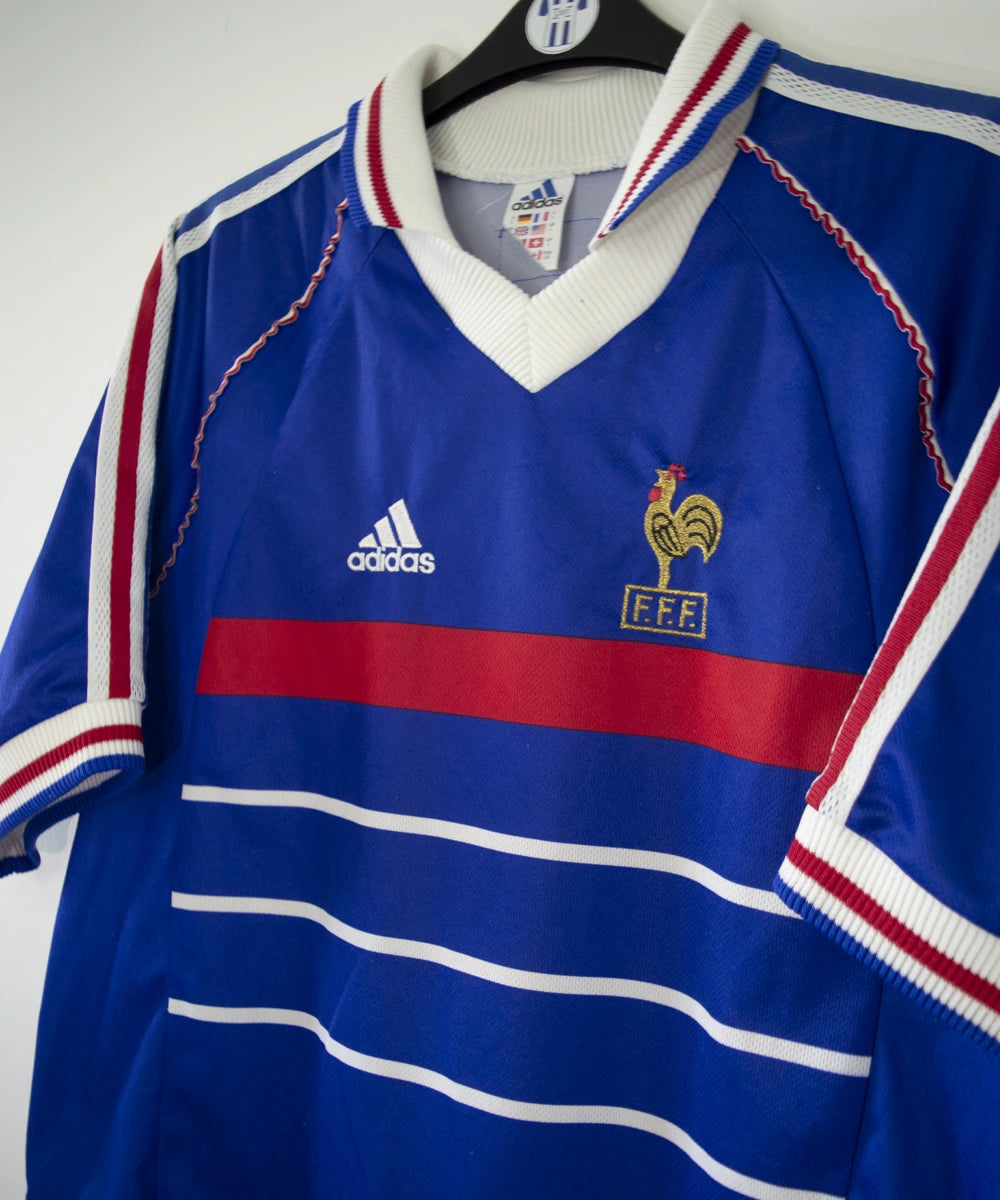 Maillot de foot vintage bleu, blanc et rouge de l'équipe de france 1998. On peut retrouver l'équipementier adidas. Il s'agit d'un maillot authentique édité avant la finale de la coupe du monde car celui-ci ne possède pas l'étoile.