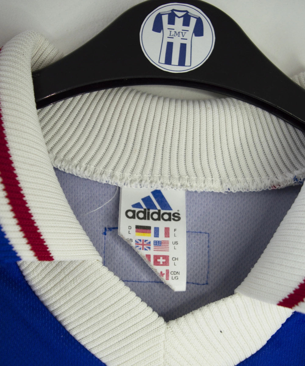 Maillot de foot vintage bleu, blanc et rouge de l'équipe de france 1998. On peut retrouver l'équipementier adidas. Il s'agit d'un maillot authentique édité avant la finale de la coupe du monde car celui-ci ne possède pas l'étoile.