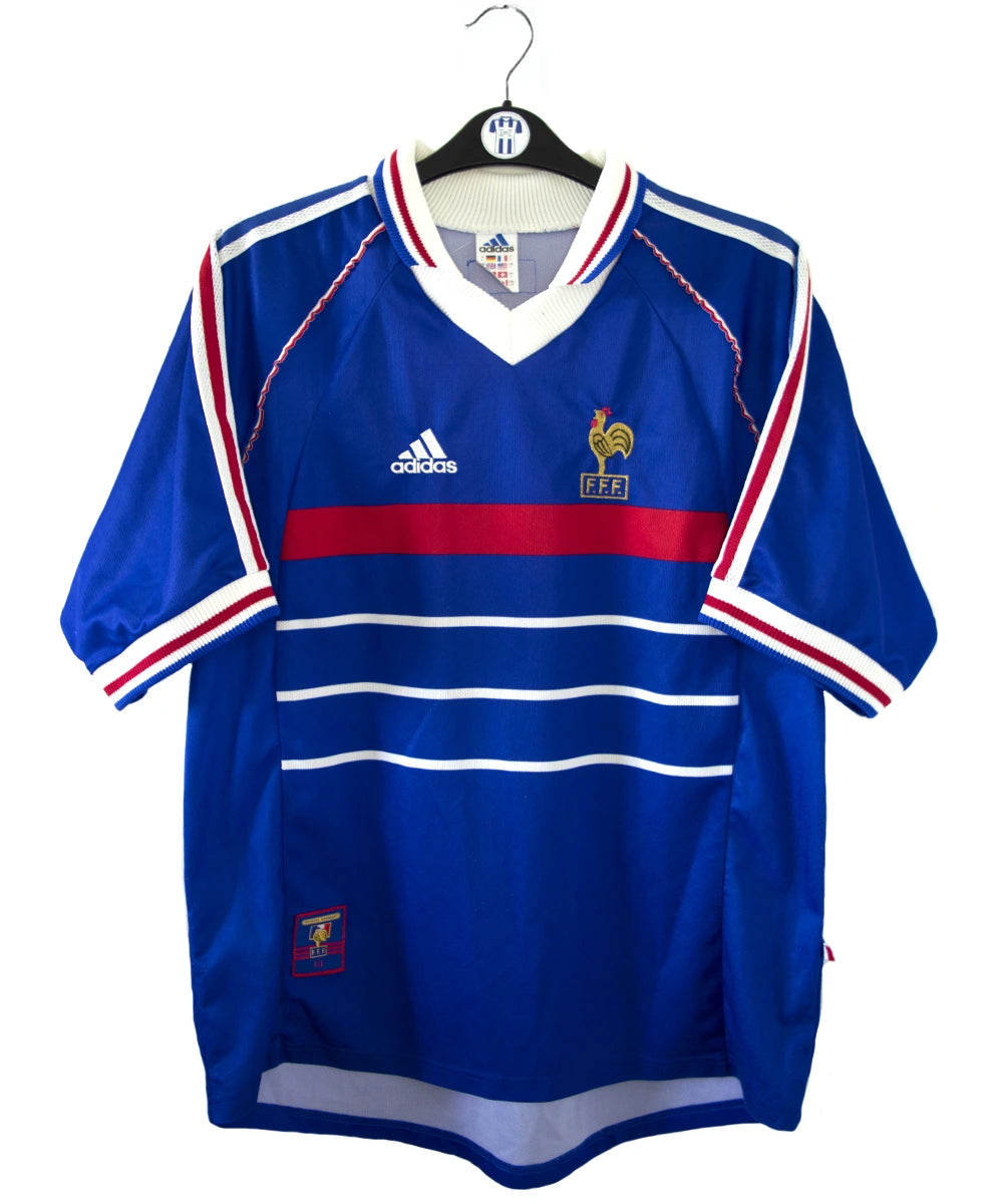Maillot de foot vintage bleu, blanc et rouge de l'équipe de france 1998. On peut retrouver l'équipementier adidas. Il s'agit d'un maillot authentique édité avant la finale de la coupe du monde car celui-ci ne possède pas l'étoile. Le maillot possède la mention pour toi avec la signature de zidane
