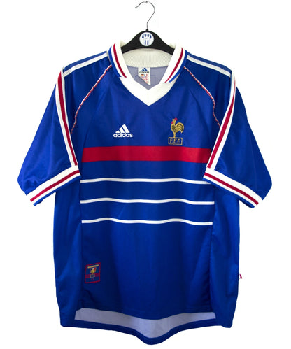 Maillot de foot vintage bleu, blanc et rouge de l'équipe de france 1998. On peut retrouver l'équipementier adidas. Il s'agit d'un maillot authentique édité avant la finale de la coupe du monde car celui-ci ne possède pas l'étoile. Le maillot possède la mention pour toi avec la signature de zidane