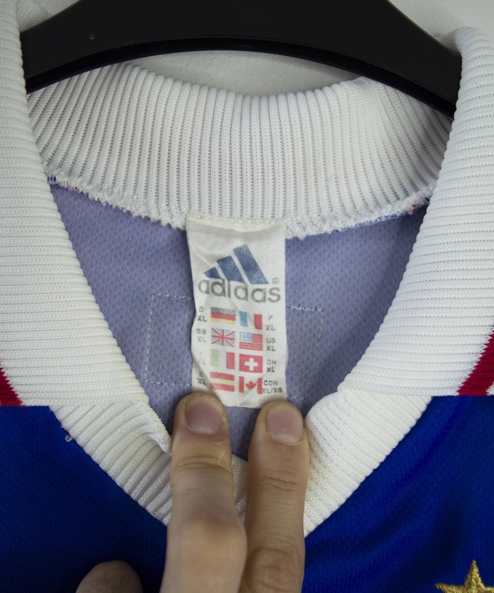 Maillot de foot vintage domicile bleu, blanc et rouge de l'équipe de france 1998. On peut voir l'équipementier adidas. Le maillot est floqué du numéro 10 Zidane. Il s'agit d'un maillot authentique d'époque