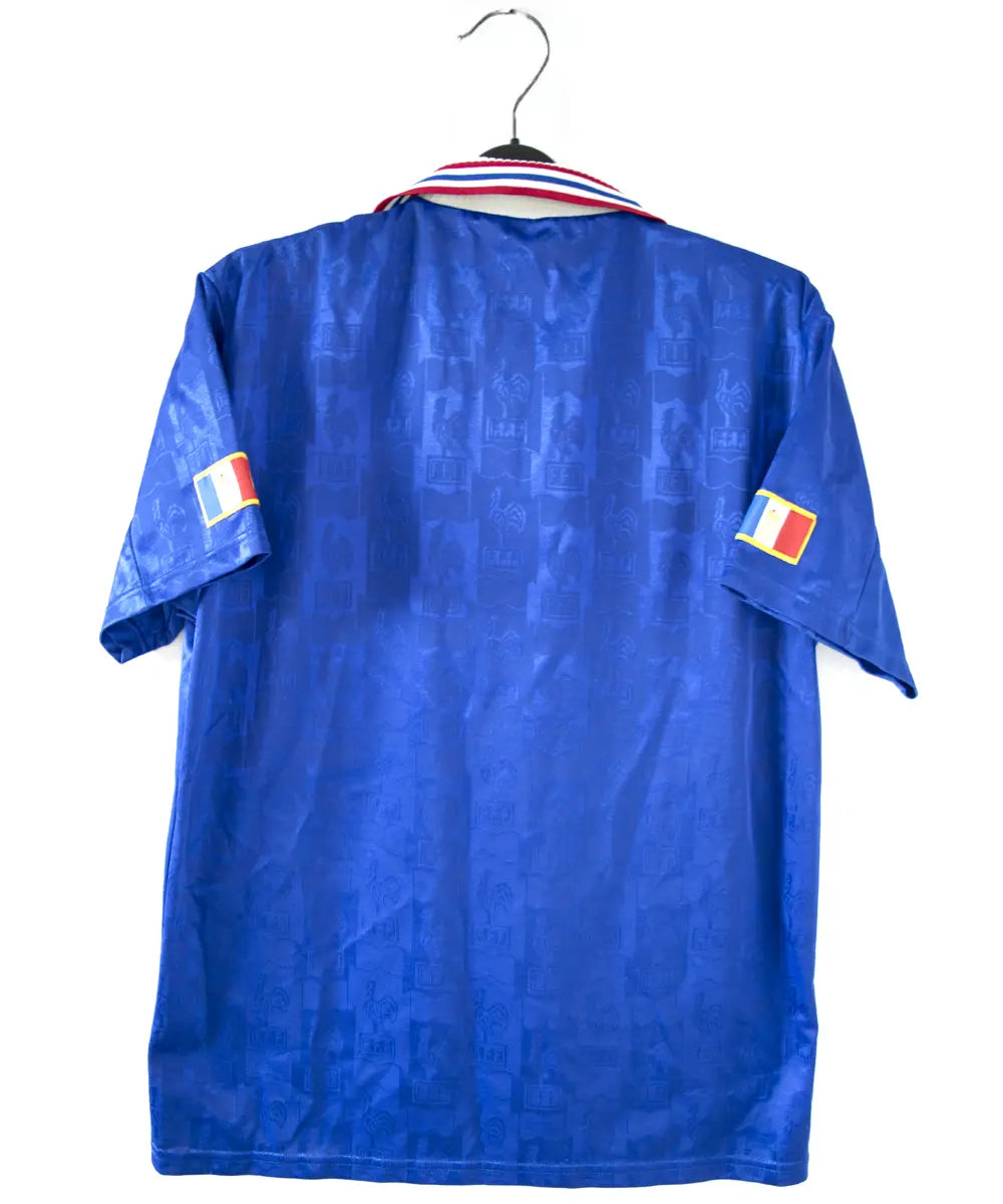 Maillot domicile bleu blanc et rouge de l'équipe de france 1996. On peut retrouver l'équipementier adidas et le coq sans l'étoile.