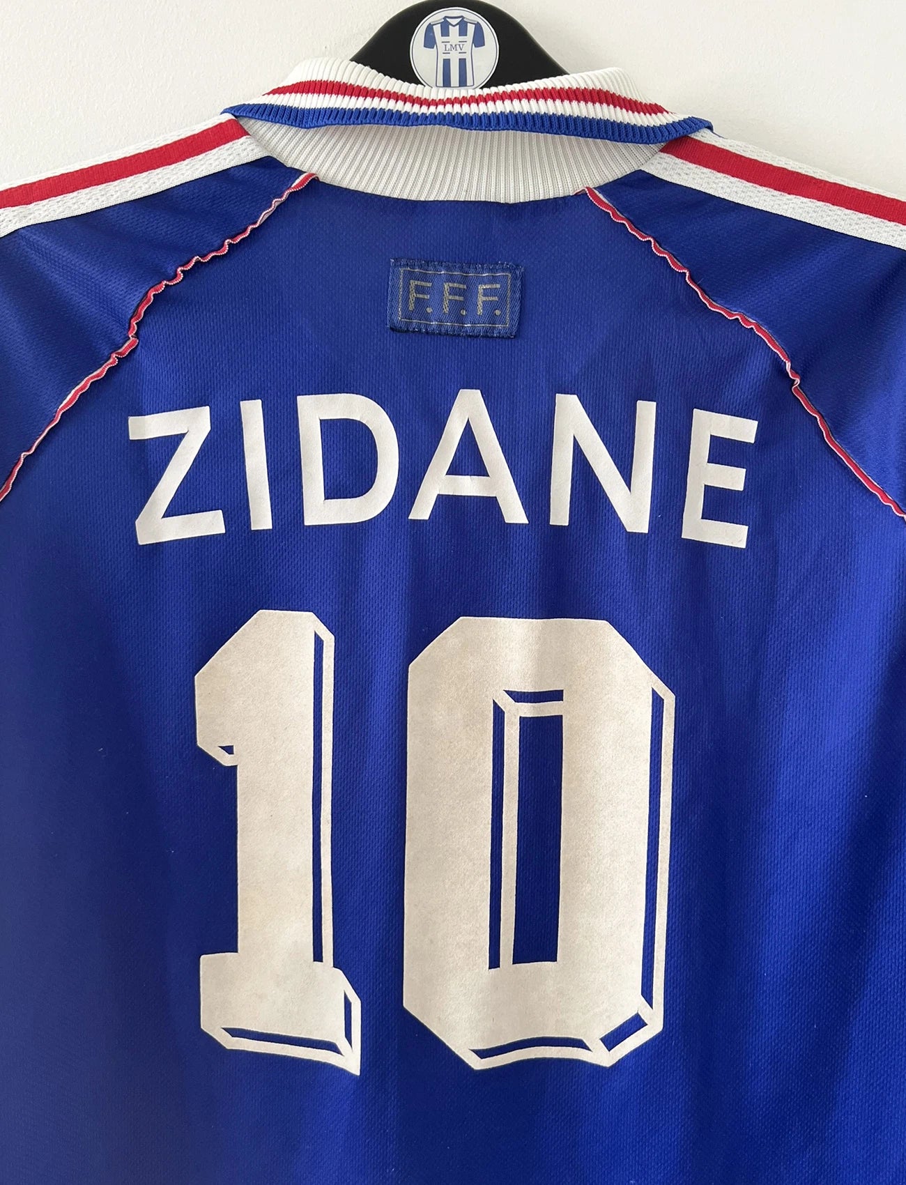 Maillot de foot vintage bleu, blanc et rouge de l'équipe de france 1998. On peut retrouver l'équipementier adidas. Il s'agit d'un maillot authentique édité avant la finale de la coupe du monde car celui-ci ne possède pas l'étoile. Le maillot est floqué du numéro 10 Zidane