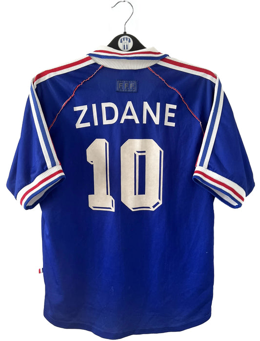 Maillot de foot vintage bleu, blanc et rouge de l'équipe de france 1998. On peut retrouver l'équipementier adidas. Il s'agit d'un maillot authentique édité avant la finale de la coupe du monde car celui-ci ne possède pas l'étoile. Le maillot est floqué du numéro 10 Zidane