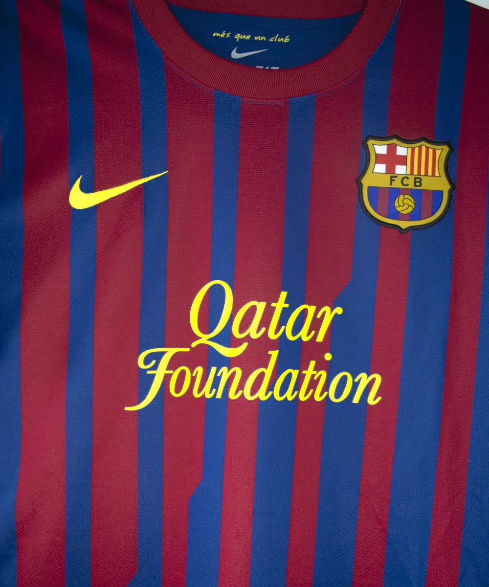 Maillot domicile bleu et rouge du fc barcelone de la saison 2011-2012. On peut retrouver le sponsor qatar foundation, le sponsor unicef et l'équipementier nike. Le maillot est floqué du numéro 10 Leo Messi. Sur cette photo on peut voir le devant du maillot de près