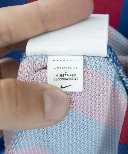 Maillot domicile bleu et rouge du fc barcelone de la saison 2011-2012. On peut retrouver le sponsor qatar foundation, le sponsor unicef et l'équipementier nike. Le maillot est floqué du numéro 10 Leo Messi. Sur cette photo on peut voir l"étiquette d'authenticité comportant les numéros 419877-486