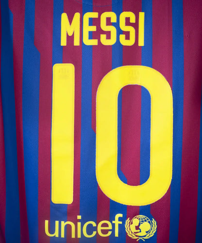 Maillot domicile bleu et rouge du fc barcelone de la saison 2011-2012. On peut retrouver le sponsor qatar foundation, le sponsor unicef et l'équipementier nike. Le maillot est floqué du numéro 10 Leo Messi. Sur cette photo on peut voir le flocage de près