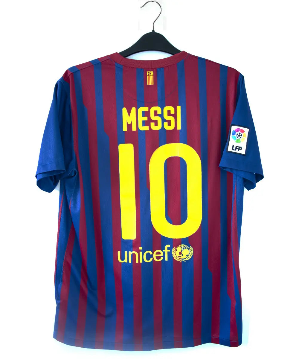 Maillot domicile bleu et rouge du fc barcelone de la saison 2011-2012. On peut retrouver le sponsor qatar foundation, le sponsor unicef et l'équipementier nike. Le maillot est floqué du numéro 10 Leo Messi. Sur cette photo on peut voir le flocage