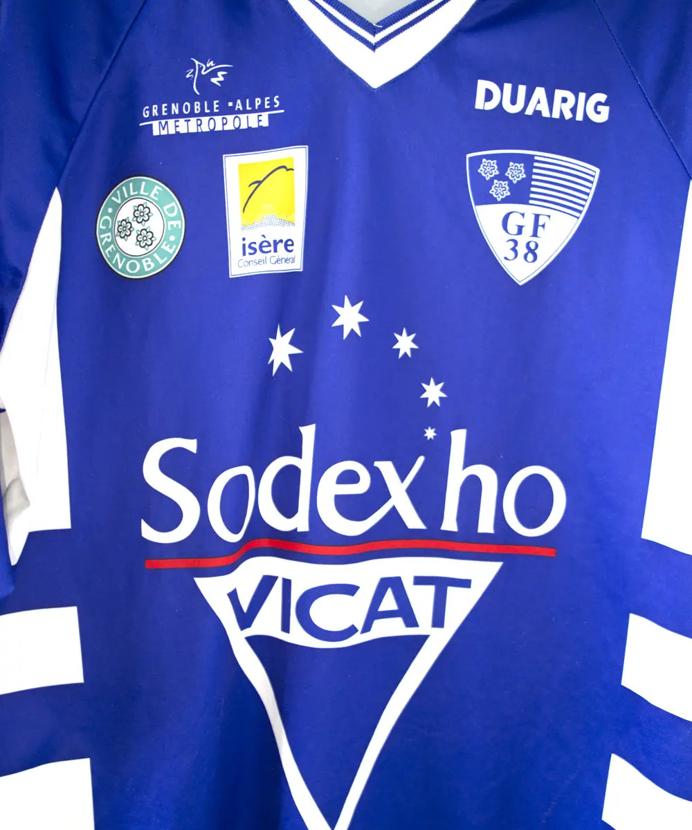 Maillot domicile de grenoble de la saison 1999/2000 de près. On peut retrouver l'équipementier duarig et le sponsor sodexo. Le maillot est de couleur bleu et blanc.