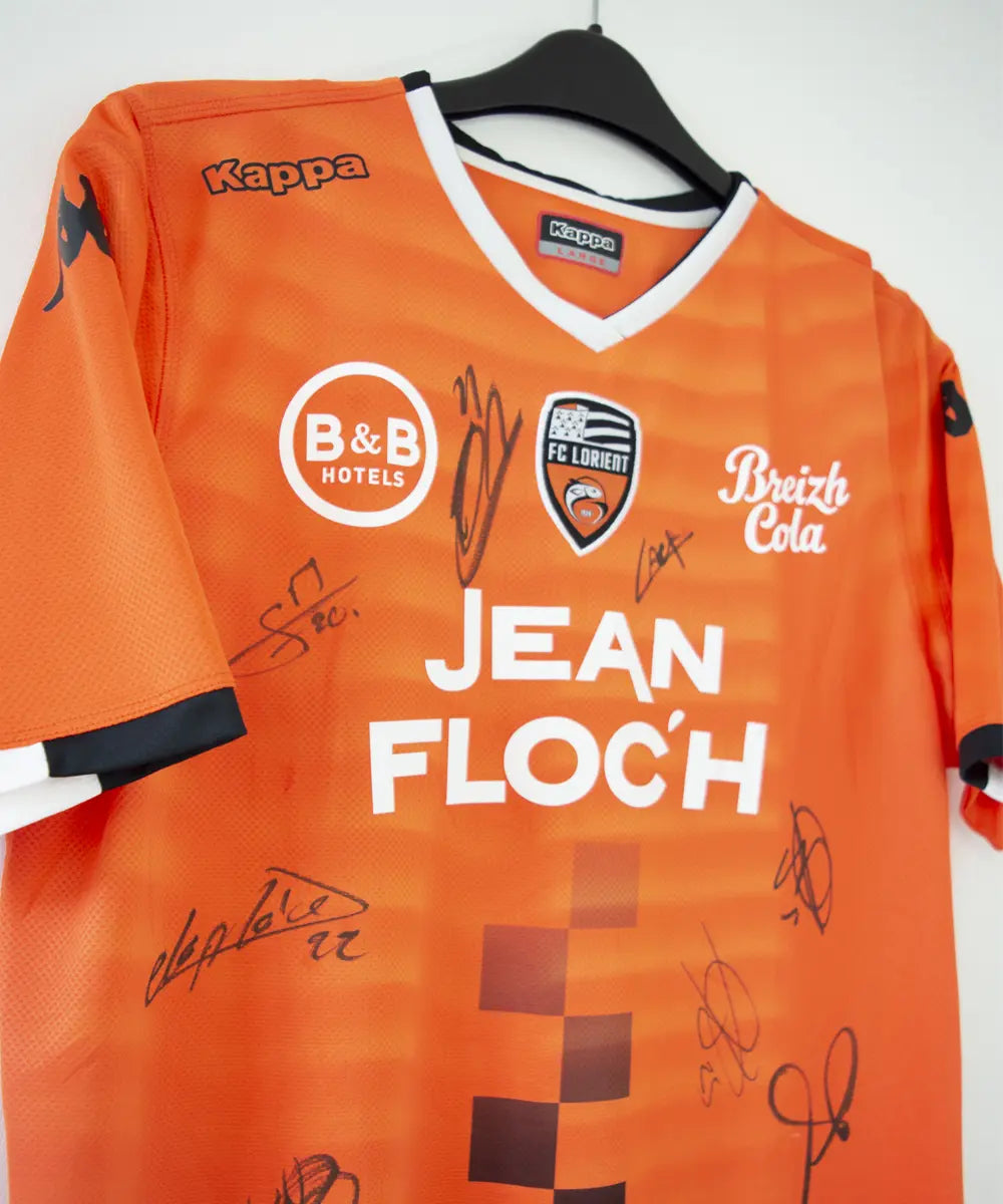 Maillot domicile de Lorient de la saison 2018-2019 de couleur orange, blanc et noir. On peut retrouver l'équipementier kappa et les sponsors jean floc'h, b&b et breizh cola. Le maillot est floqué du numéro 22 delaplace et signé par plusieurs joueurs de l'équipe