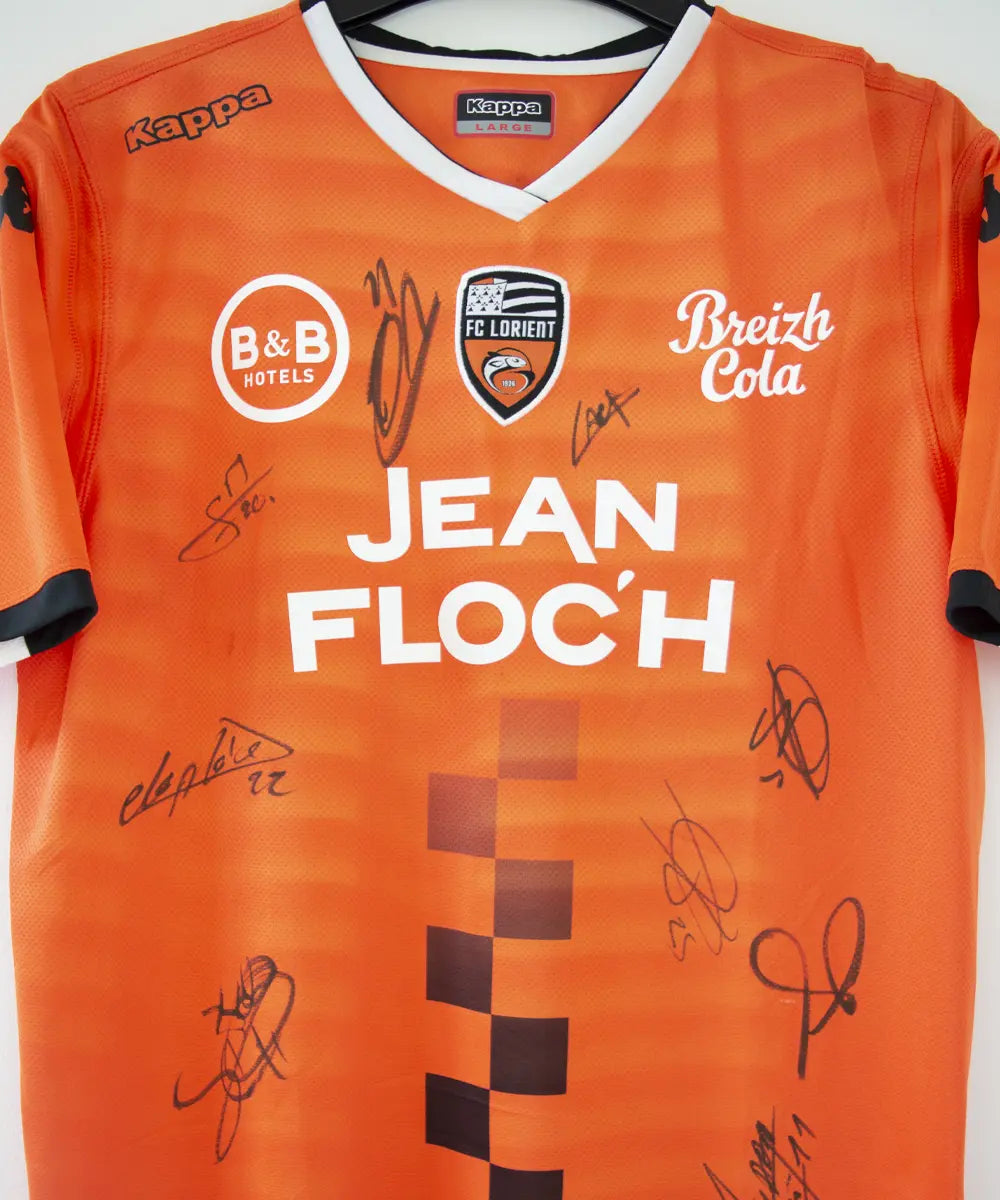 Maillot domicile de Lorient de la saison 2018-2019 de couleur orange, blanc et noir. On peut retrouver l'équipementier kappa et les sponsors jean floc'h, b&b et breizh cola. Le maillot est floqué du numéro 22 delaplace et signé par plusieurs joueurs de l'équipe